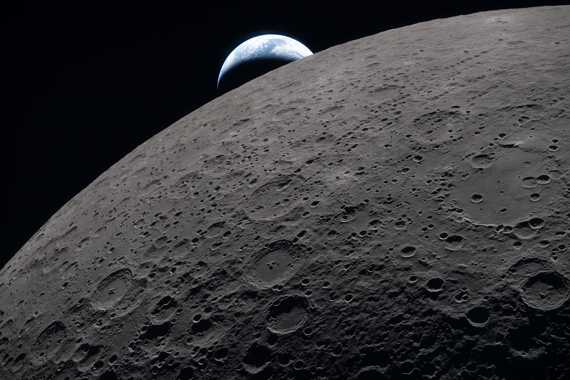 The lunar surface fills the frame in sharp detail, as seen during the Artemis II lunar flyby, while a distant Earth sets in the background. This image was captured at 6:41 p.m. EDT, on April 6, 2026, just three minutes before the Orion spacecraft and its crew went behind the Moon and lost contact with Earth for 40 minutes before emerging on the other side. In this image, the dark portion of Earth is experiencing nighttime, while on its day side, swirling clouds are visible over the Australia and Oceania region. In the foreground, Ohm crater shows terraced edges and a relatively flat floor marked by central peaks - formed when the surface rebounded upward during the impact that created the crater.